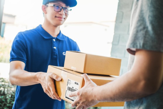 A GLS driver hands packages to a customer, with only the customer’s arms visible.